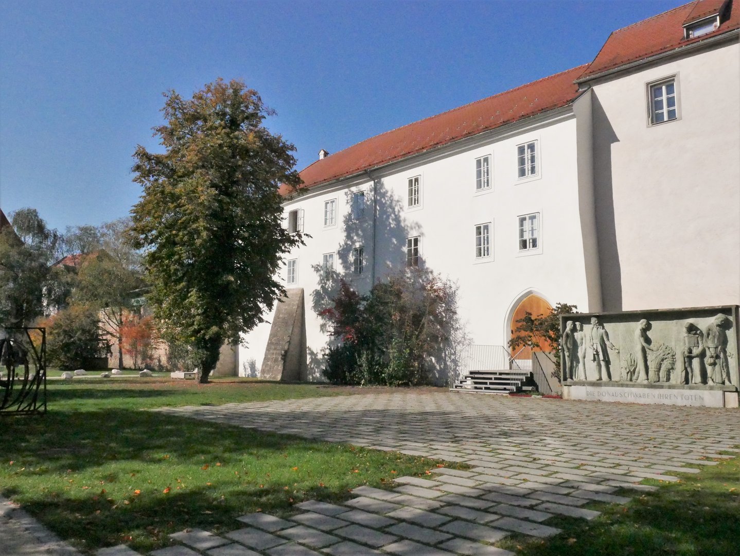 Außenansicht des Minoritenklosters Wels mit rotem Dach, Eingangsportal und Vorplatz
